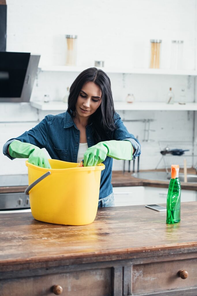 Pleased woman in rubber gloves using plastic bucket in kitchen